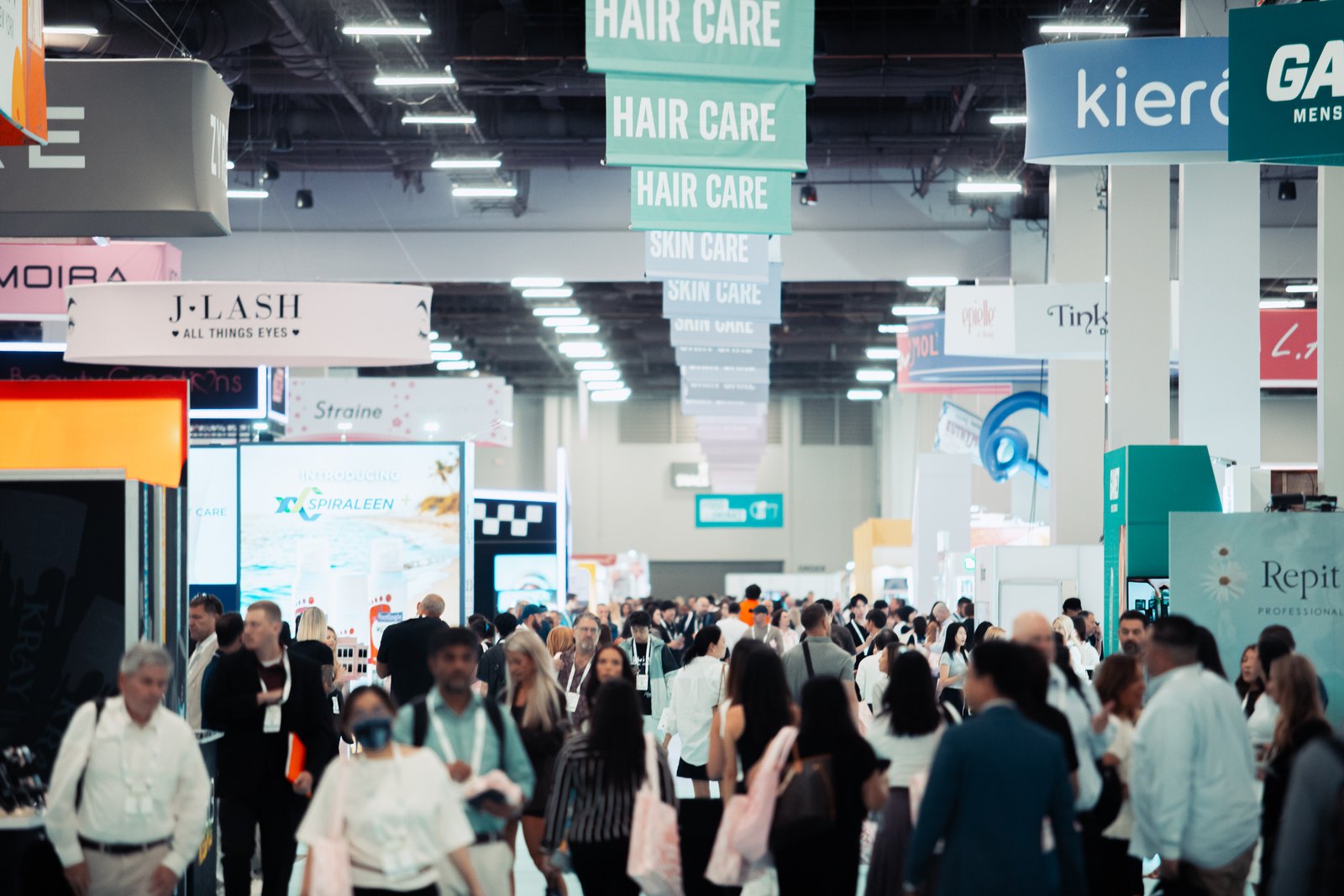 Overhead HAIR CARE and SKIN CARE aisle signage above a crowded Cosmoprof show floor